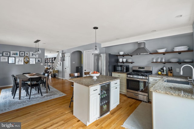 kitchen featuring arched walkways, beverage cooler, open shelves, appliances with stainless steel finishes, and wall chimney exhaust hood