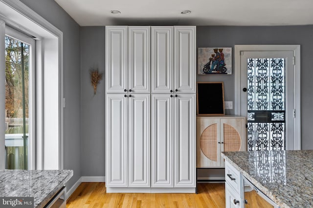 kitchen with light stone counters, white cabinetry, light wood-style floors, and baseboards