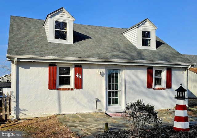 cape cod-style house featuring a patio area, roof with shingles, and stucco siding