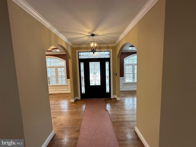 foyer featuring dark wood-style floors, arched walkways, crown molding, and an inviting chandelier