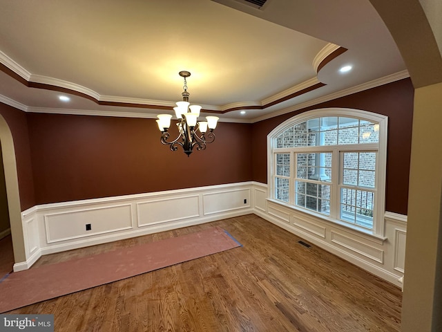 unfurnished dining area with arched walkways, wood finished floors, visible vents, a raised ceiling, and an inviting chandelier