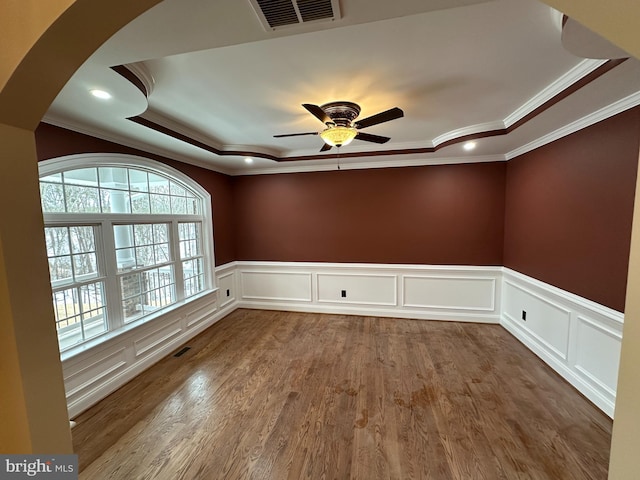 unfurnished room with a tray ceiling, visible vents, ceiling fan, and wood finished floors