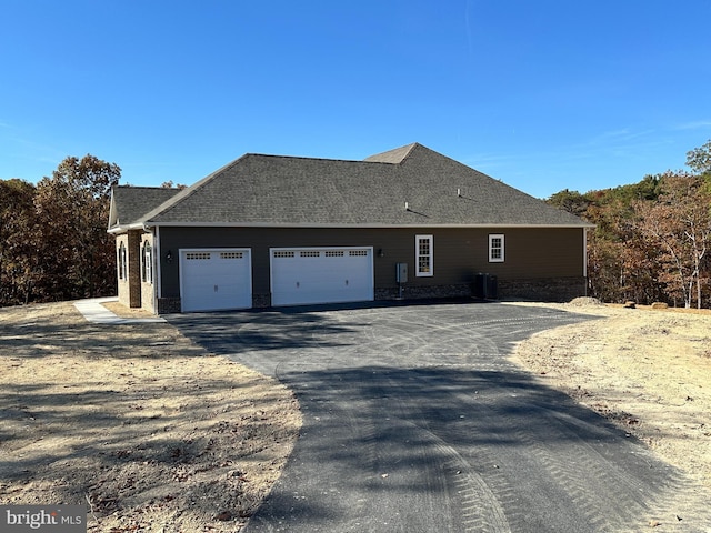 view of side of property with roof with shingles, driveway, and an attached garage