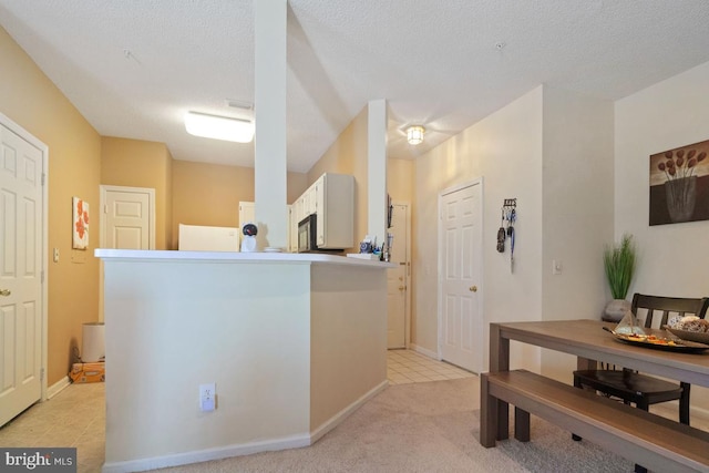 interior space featuring black microwave, light tile patterned floors, white cabinetry, and a textured ceiling