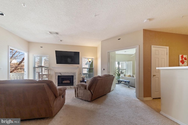 living area featuring a textured ceiling, light carpet, a premium fireplace, visible vents, and baseboards