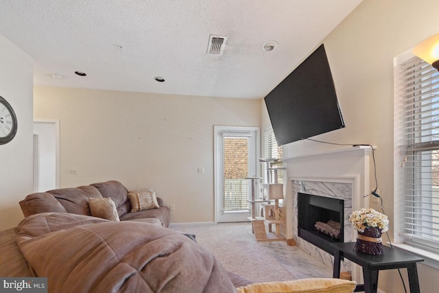 carpeted living room featuring a textured ceiling, a fireplace, visible vents, and baseboards