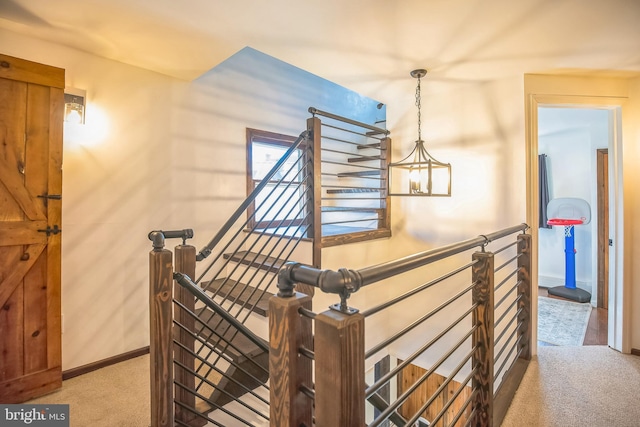 hall featuring an inviting chandelier, baseboards, carpet flooring, and an upstairs landing