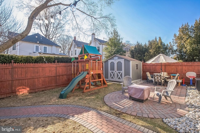 view of jungle gym featuring a fenced backyard, an outbuilding, outdoor dining area, a patio area, and a shed