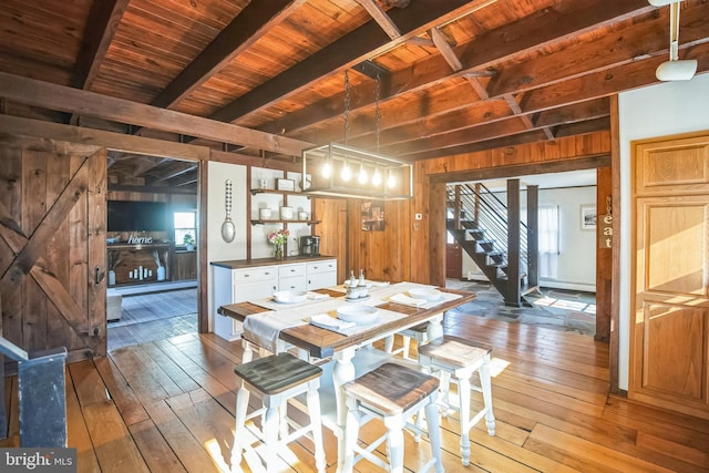 dining room featuring wooden walls, stairway, a wealth of natural light, beam ceiling, and wood-type flooring