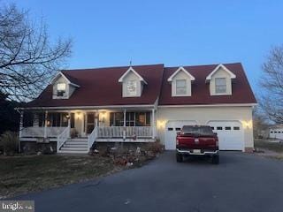 new england style home featuring a garage, a porch, and aphalt driveway