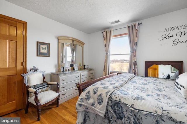 bedroom with light wood-style floors, multiple windows, visible vents, and a textured ceiling