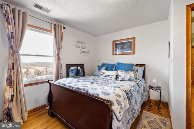 bedroom with light wood finished floors, baseboards, visible vents, and a textured ceiling