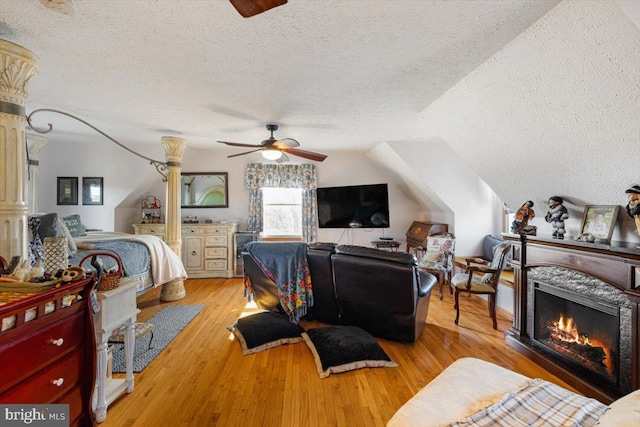 bedroom featuring lofted ceiling, light wood-style flooring, a textured ceiling, and a glass covered fireplace