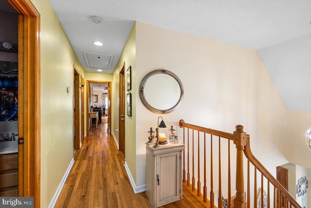 hall featuring attic access, baseboards, wood finished floors, and an upstairs landing