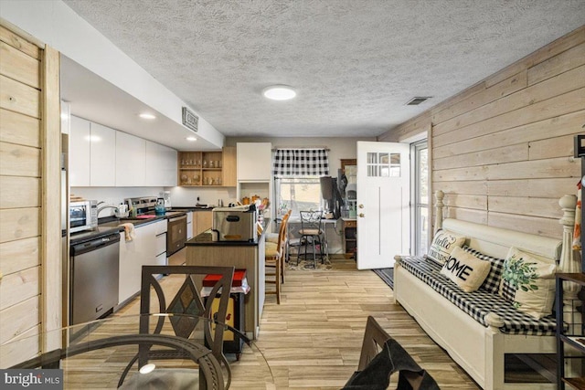 kitchen featuring stainless steel dishwasher, range with electric cooktop, dark countertops, and visible vents