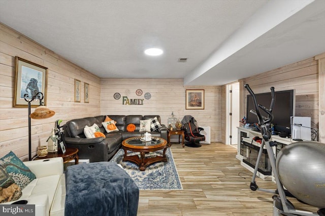 living area with visible vents, wood walls, a textured ceiling, and wood finished floors