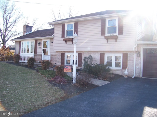 tri-level home with a garage, a chimney, a front lawn, and brick siding