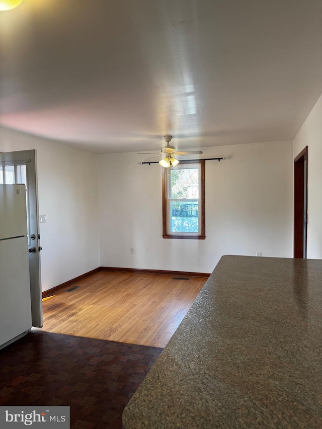 unfurnished room with ceiling fan, wood finished floors, and baseboards