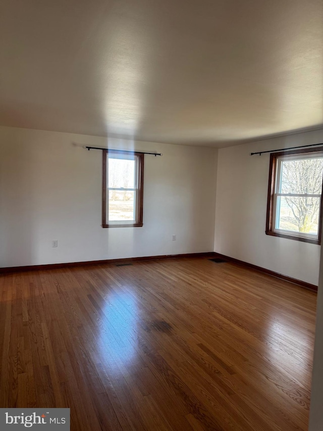 spare room with a healthy amount of sunlight, baseboards, and wood finished floors