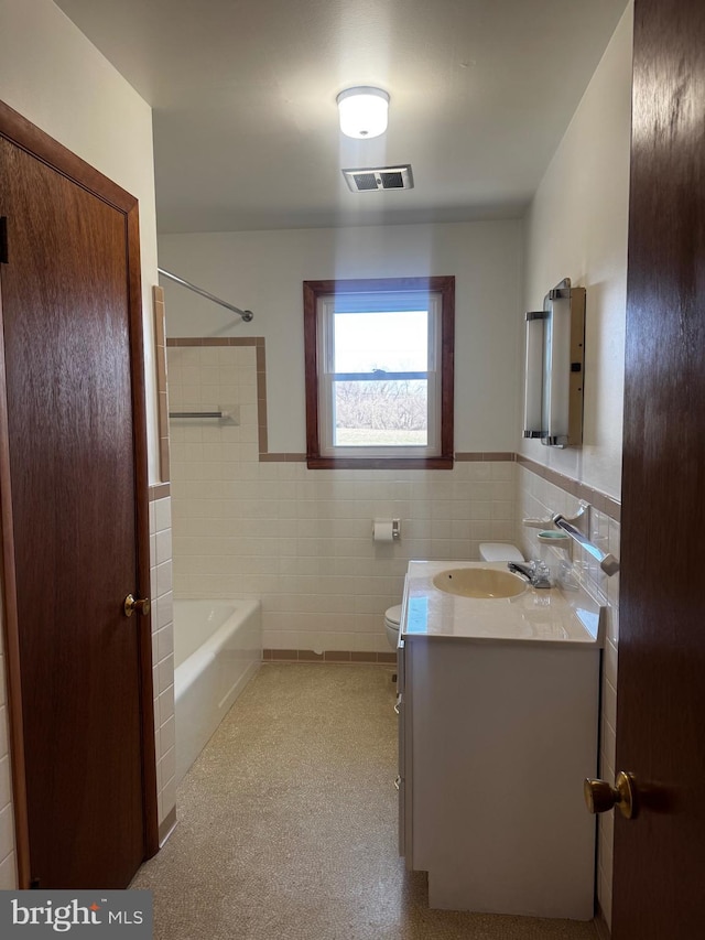 bathroom with visible vents, bathing tub / shower combination, toilet, vanity, and tile walls