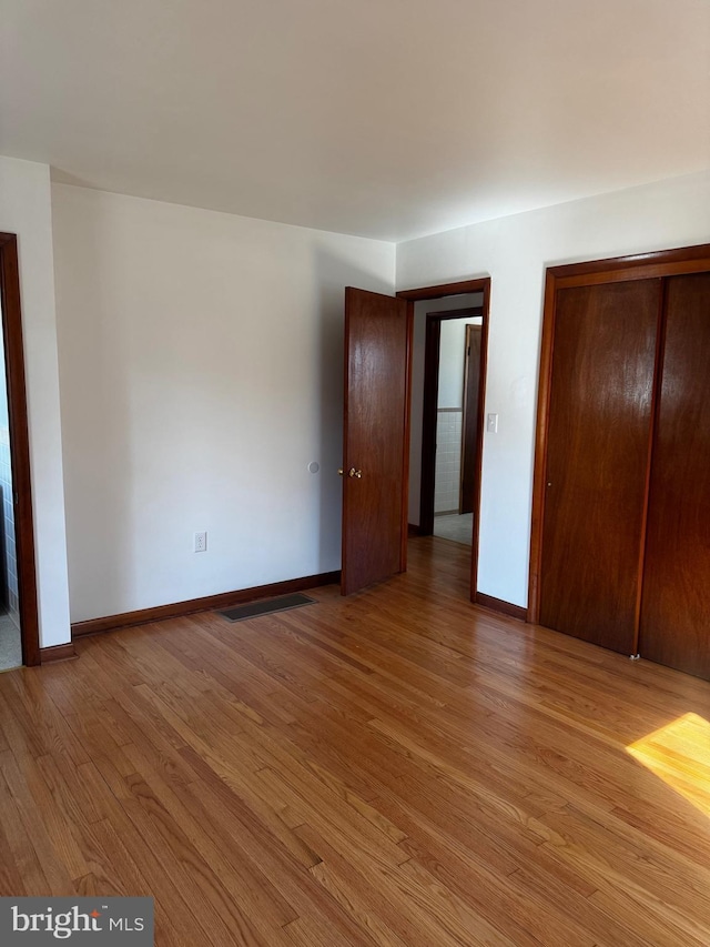 unfurnished bedroom with light wood-type flooring, visible vents, baseboards, and a closet