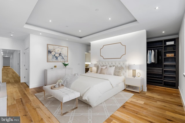 bedroom with a raised ceiling, hardwood / wood-style flooring, recessed lighting, and a closet