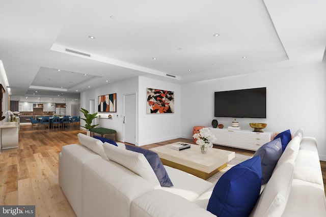 living room featuring visible vents, a raised ceiling, baseboards, light wood-style flooring, and recessed lighting