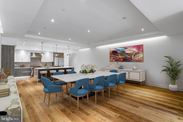 dining room featuring light wood-type flooring, baseboards, a tray ceiling, and recessed lighting