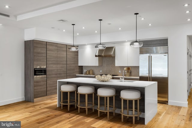 kitchen featuring visible vents, wall chimney exhaust hood, modern cabinets, stainless steel appliances, and a sink