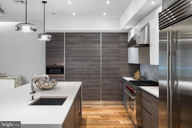 kitchen with premium appliances, light countertops, a sink, wall chimney range hood, and modern cabinets