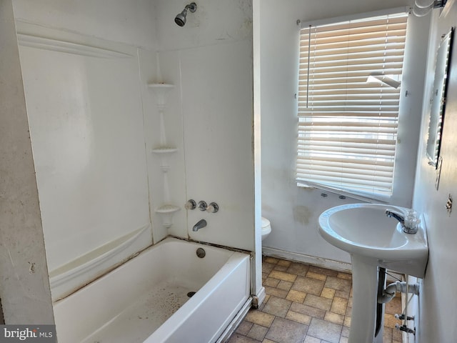 bathroom with bathtub / shower combination, toilet, stone finish floor, a sink, and baseboards