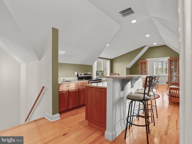 kitchen with plenty of natural light, visible vents, a kitchen bar, electric stove, and light wood finished floors