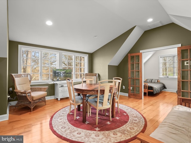 dining space with baseboards, light wood-style flooring, visible vents, and vaulted ceiling