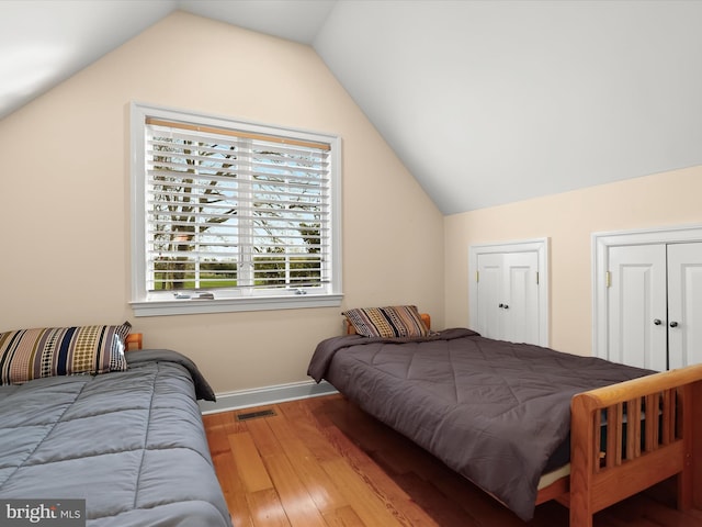 bedroom featuring visible vents, baseboards, wood finished floors, and lofted ceiling
