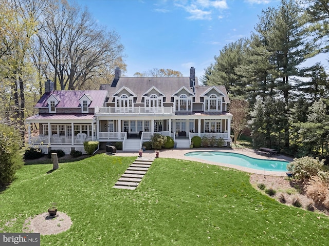 rear view of property featuring a balcony, a chimney, an outdoor pool, a porch, and a yard