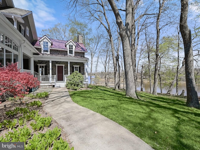 exterior space featuring a water view, a porch, a lawn, and a chimney
