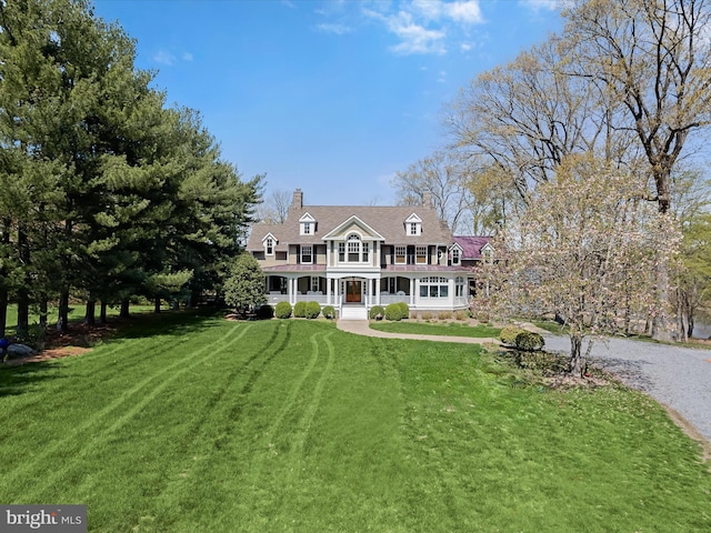 view of front facade with a porch, a chimney, a balcony, a front lawn, and gravel driveway