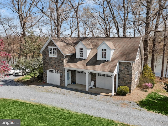 view of front facade featuring stone siding, a garage, and gravel driveway