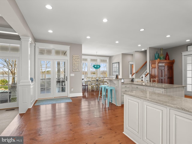 kitchen with an island with sink, white cabinetry, recessed lighting, ornate columns, and light wood-style flooring
