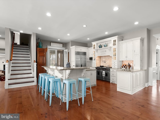 kitchen featuring high end appliances, an island with sink, wood-type flooring, and white cabinets