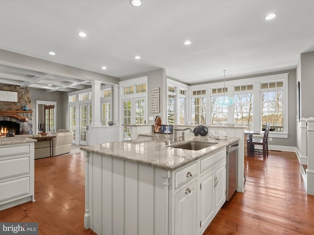 kitchen with hardwood / wood-style floors, dishwasher, a sink, and a center island with sink