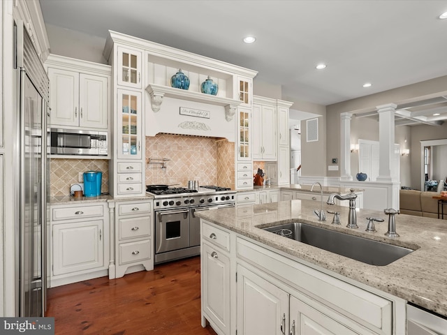 kitchen with tasteful backsplash, built in appliances, a sink, dark wood-style flooring, and white cabinetry