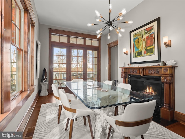 dining area featuring baseboards, an inviting chandelier, a glass covered fireplace, and dark wood-style floors