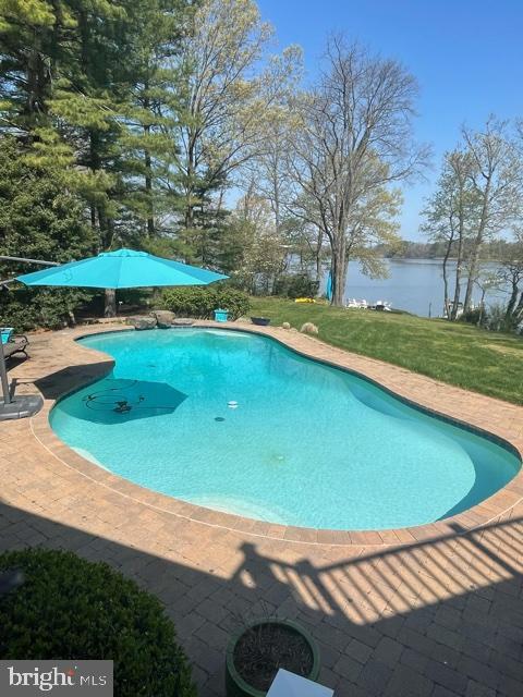 pool featuring a water view, a patio, and a yard