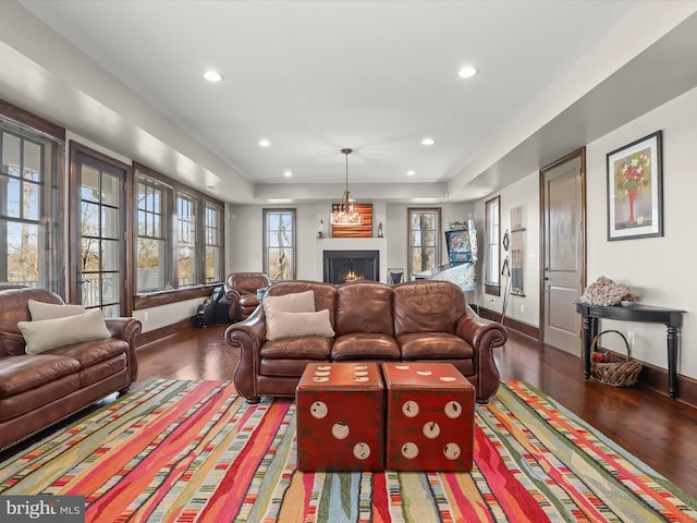 living room featuring a tray ceiling, a warm lit fireplace, recessed lighting, wood finished floors, and baseboards