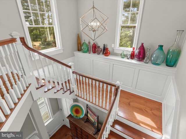 stairs with a chandelier, a decorative wall, and wood finished floors