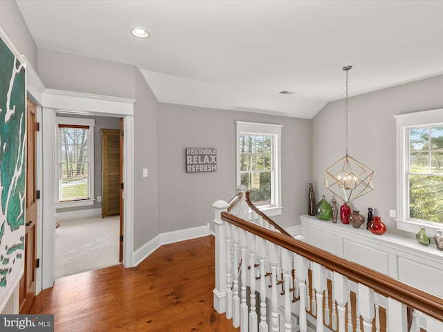 corridor featuring plenty of natural light, an upstairs landing, a notable chandelier, and wood finished floors