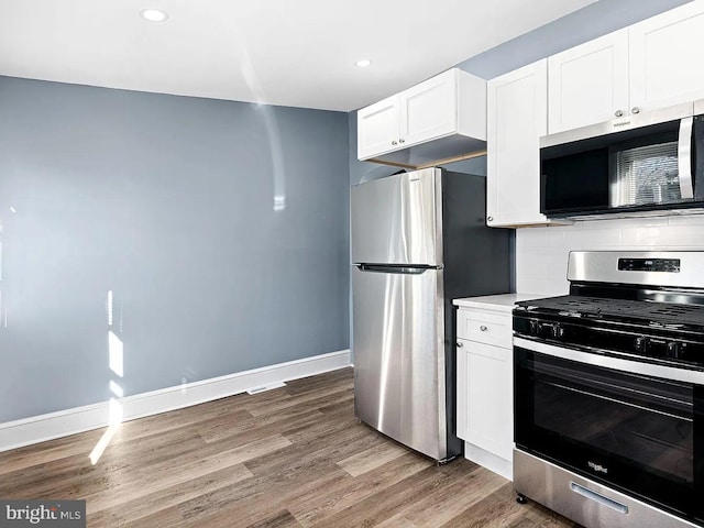 kitchen featuring baseboards, white cabinets, stainless steel appliances, light countertops, and light wood-type flooring