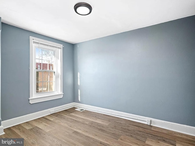 unfurnished room featuring visible vents, baseboards, and wood finished floors