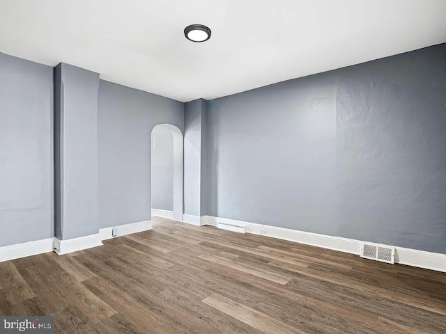 spare room with arched walkways, visible vents, baseboards, and wood finished floors